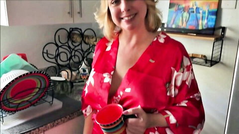 Blonde MILF with huge tits flashes deep cleavage in open red silk robe holding mugs in kitchen