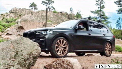 Matte black BMW X7 SUV parked on rocky outdoor terrain surrounded by pines