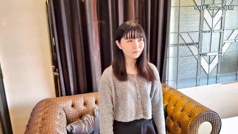 Cute Asian babe in gray cardigan and skirt stands teasingly