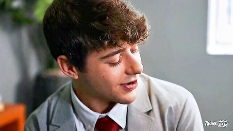 Handsome young brunette twink in gray suit and red tie smiling seductively