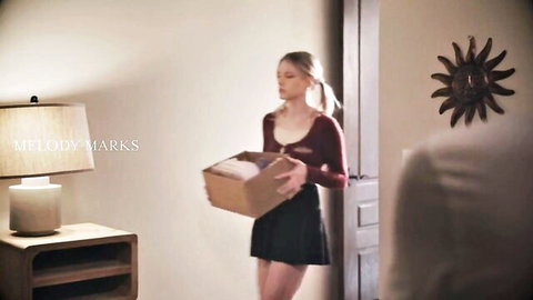 Blonde teen Melody Marks in red top and black mini skirt holding a box