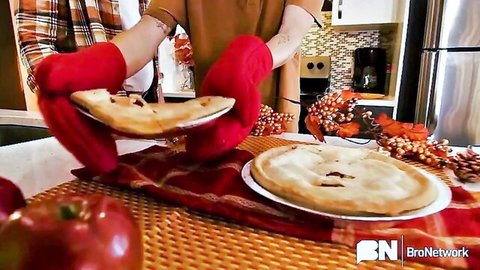 Woman in plaid shirt holding two steaming hot pies fresh from oven with red mitts in festive kitchen