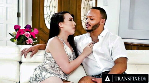 Brunette trans woman passionately kissing black stud on couch with hand on his chest