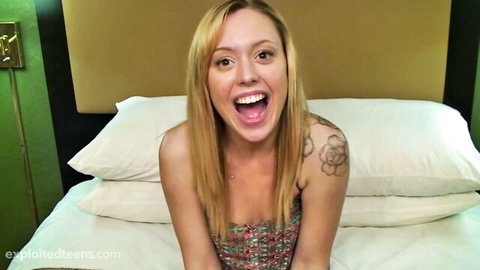 Blonde teen Lucy Tyler smiling excitedly on bed in colorful top
