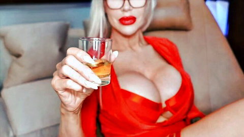Busty blonde in tight red dress flaunts massive cleavage holding whiskey glass seductively.