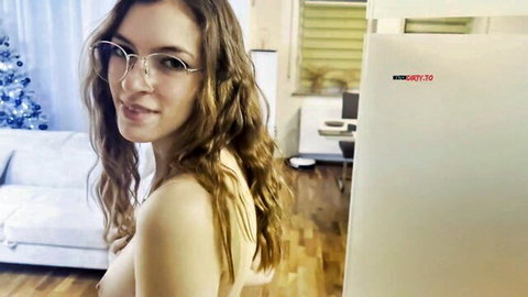 Nude brunette with glasses smirks over shoulder showing bare back and side tits