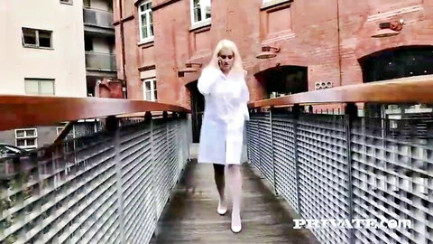 Blonde nurse babe in short white dress and stockings walks seductively on urban metal walkway