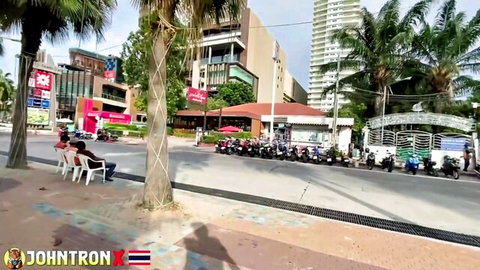 Busy Thai street scene with parked scooters palm trees and people sitting on white chairs outdoors