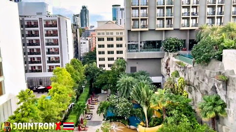 Panoramic view of Bangkok hotel infinity pool surrounded by high-rises tropical greenery and Thai flags