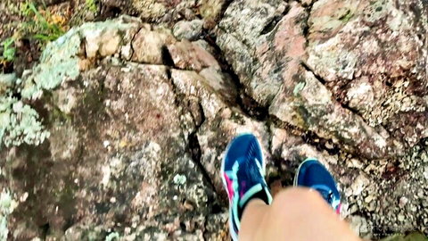 POV closeup of woman's sexy feet in blue sneakers stepping on mossy jungle rocks