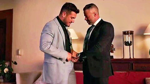 Two suited handsome men intimately adjusting watch in hotel room gay foreplay tease