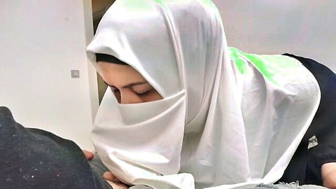 Seductive niqab-clad Arab woman with green-stained white hijab leans down eyes up in teasing POV blowjob pose