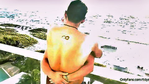 Two hot tattooed muscular studs embracing nude on balcony overlooking ocean