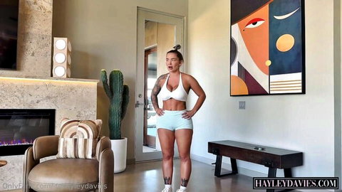 Hayley Davies posing in tight white bralette and shorts, curvy tattooed body