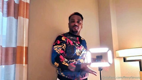Angel Luv OnlyFans promo: Black man in colorful sweater holding ring light, smiling