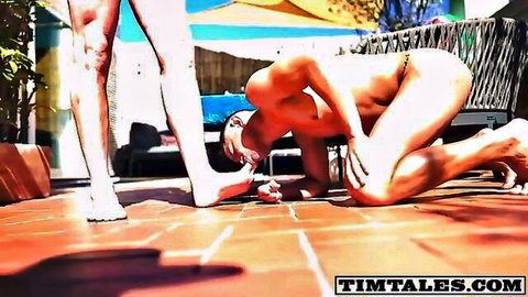 Muscular man kneels nude worshipping woman's feet in dominating outdoor scene