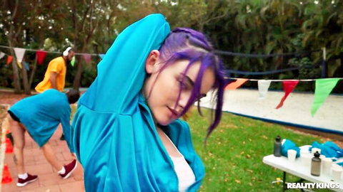 Cherie DeVille stretches in blue tracksuit, purple hair outdoors