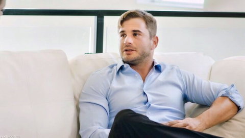 Handsome bearded man in blue shirt and black pants sitting on white couch