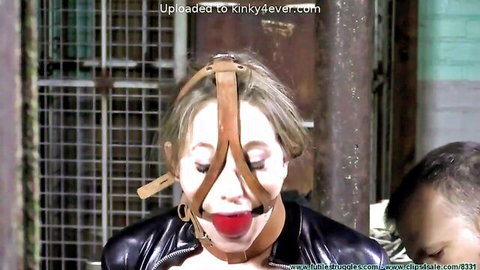 Blonde MILF gagged with red ball in leather BDSM harness dominated in dungeon cell