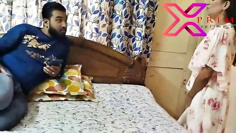 Bearded Indian man on bed eyeing sexy wife in pink floral dress standing by door