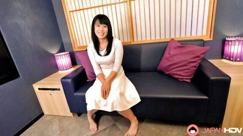 Cute Japanese woman in white skirt sits on couch with legs spread smiling teasingly
