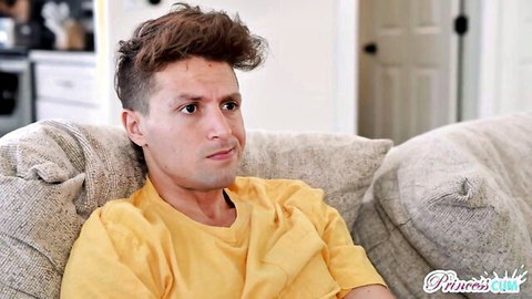 Young man with curly brown hair sits on beige couch wearing yellow t-shirt in cozy living room