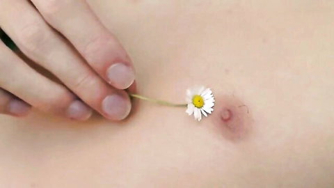 Hand holding daisy flower on pale bare skin near mole, soft intimate close-up