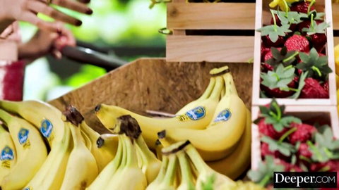 Cluster of thick ripe yellow bananas with blue labels and juicy red strawberries in wooden market crate display