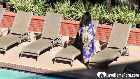 Brunette with long hair in purple robe standing by pool loungers teasing