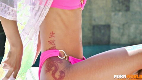 Slim Asian babe in pink O-ring bikini shows dragon tattoo on hip by pool