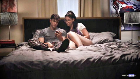 Young brunette in white panties cuddles intimately with boyfriend on bed while he scrolls phone