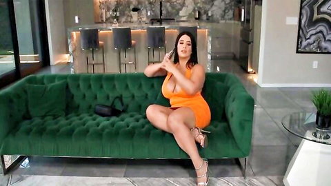 Sarah Arabic in tight orange dress, teasing cleavage on couch