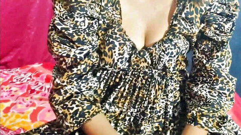 Busty South Asian babe in low-cut leopard print dress teasing deep cleavage on bed