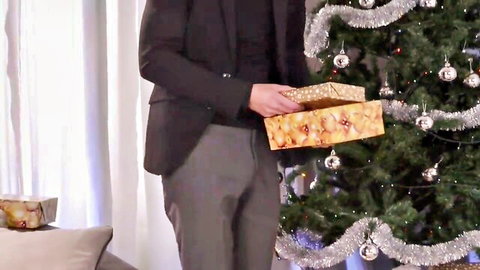 Kerry Louise in suit holding gold Christmas gift by tree