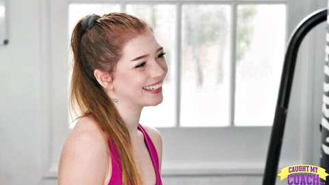 Smiling redhead teen in tight pink sports bra posing in gym
