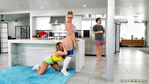 Blonde MILF bent over kitchen counter with big bare ass and shaved pussy as brunette kneels to lick her out with guy watching