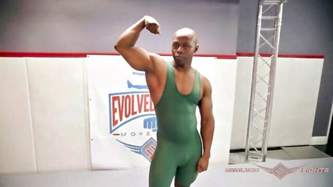 Muscular bald Black man flexing biceps in tight green EVOLVE MMA wrestling singlet