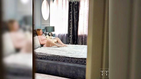 Blonde woman in pink lingerie lounging on bed with small dog