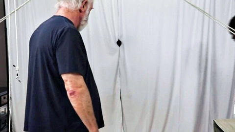 Bearded older white man stands dominating bound ebony slave in BDSM rope setup