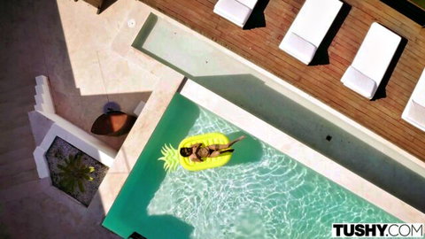 Blonde with big curvy ass in tiny black thong floats face-down on yellow pineapple in pool