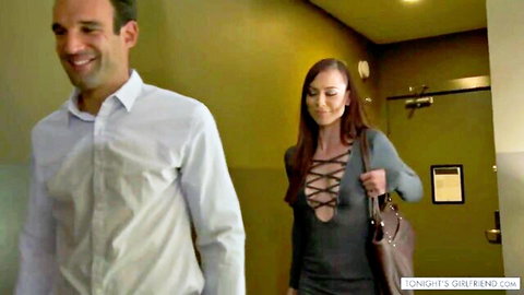 Tanned brunette girlfriend in tight lace-up dress follows smiling man in hotel hallway