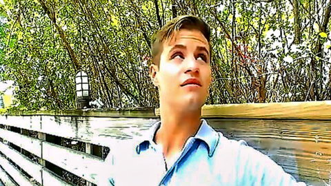 Joey Cooper gazing outdoors in open blue shirt, teasing gay hookup vibe