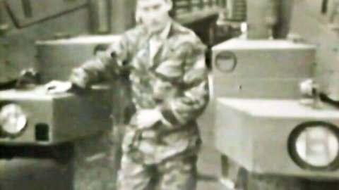 Vintage soldier in tight camo uniform posing confidently amid military equipment