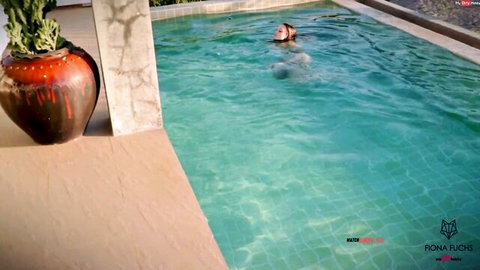 Blonde girl with long hair swims submerged in turquoise outdoor pool teasingly