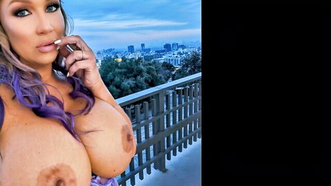 Busty purple-haired babe topless on balcony smoking cigarette with huge exposed tits and city skyline view