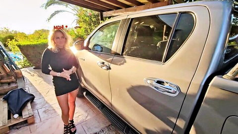 Busty blonde MILF in tight black dress teases big tits posing by silver truck