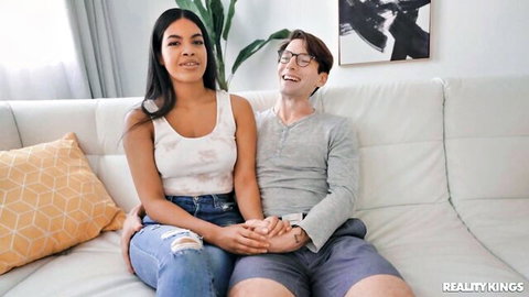Maya Farrell in tank top and jeans holds hands with partner on couch