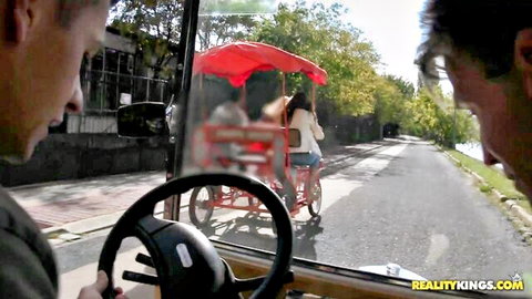 POV guys in car eyeing sexy brunette babe riding red pedicab outdoors on sunny street