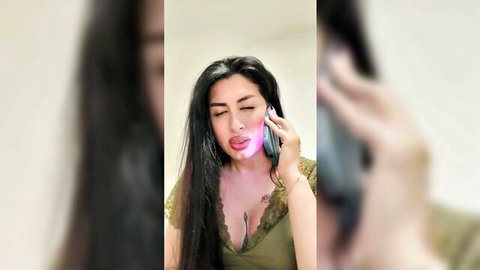 Busty South Asian woman in green lace top licks glowing phone showing deep cleavage