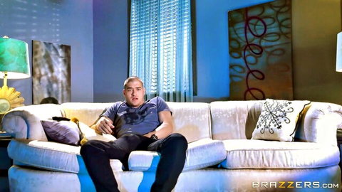 Handsome balding man in blue shirt lounging on white couch in stylish Brazzers living room